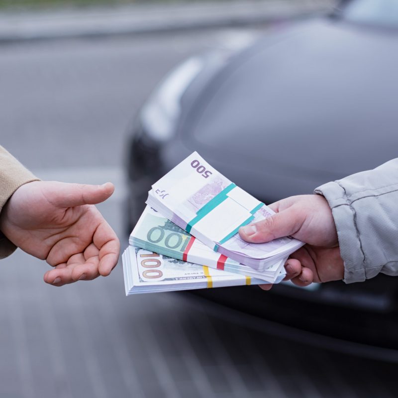 Man buys a modern car and hands over a bundle of dollars and euro to the seller